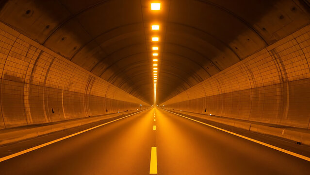 Expansive modern road tunnel illuminated by bright amber lights, creating a path towards an unknown destination