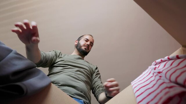 POV from inside a cardboard box of man sorting clothes for donation
