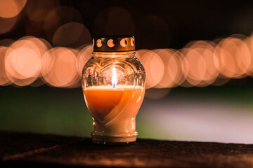 Single memorial candle burning softly in dark night with warm bokeh background.