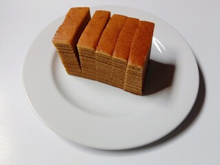 slice of lapis legit cake on plate. close-up of indonesian layer cake lapis legit slices on white plate.