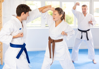 Man and woman train to perform basic defensive installations and attacking actions during combat techniques classes. Young male coach comments and corrects mistakes of students