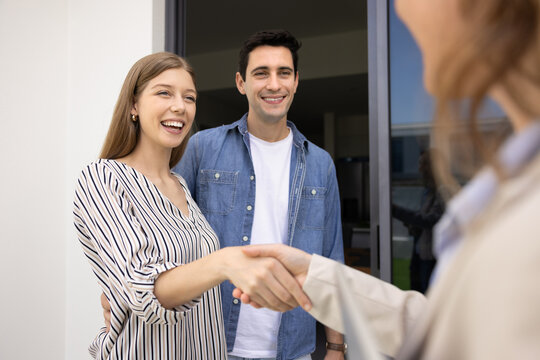 Couple stands in front of new home, handshaking with realtor