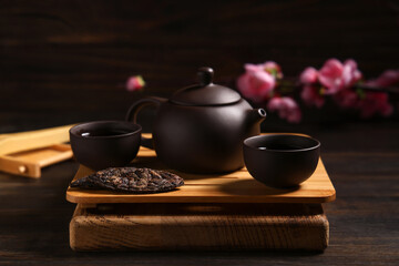 Tray with teapot, cups of tea and dry pressed puer leaves on wooden background