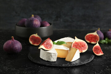 Tray with pieces of tasty Camembert cheese and fresh ripe figs on black grunge background, closeup