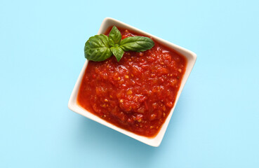 Bowl of tasty tomato sauce on blue background, closeup