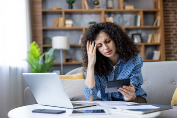 Woman feeling stressed and worried while calculating household expenses, bills, and analyzing...