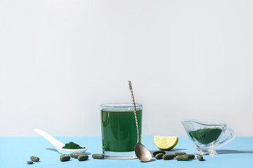 Glass of spirulina drink with pills, gravy boat, spoon, lime slice and powder on color background
