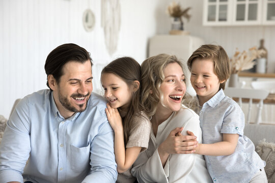 Affectionate diverse small kids snuggle close to shoulders of parents