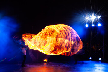 Fire Show Performance With Bright Orange Flames And Motion Trails On Dark Blue Stage Background. Creative Long Exposure