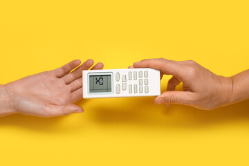 Female hands with air conditioner remote control on yellow background