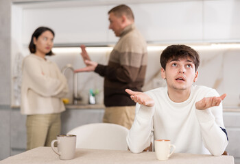 Fototapeta premium Angry young guy is tired of domestic quarrels. Relatives quarreling in the background