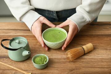Woman preparing matcha tea at wooden table in kitchen