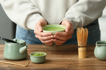Woman holding bowl of fresh matcha tea at wooden table in kitchen
