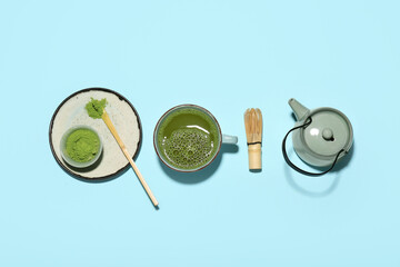 Cup of fresh matcha tea with powder, chasen, chashaku and teapot on blue background
