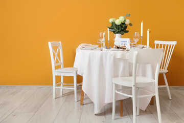 Table setting for Nobel prize day with roses and burning candles near orange wall