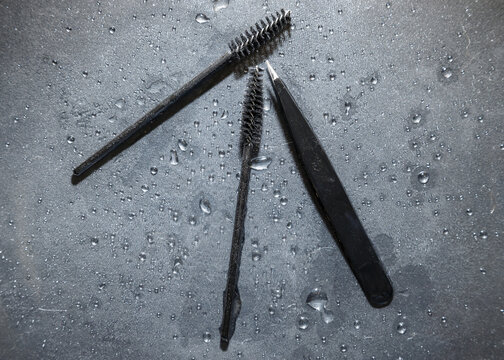 Beauty tools for eyebrow shaping and eyelash enhancement on a textured wet surface