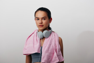 Fitness woman with towel over shoulders and headphones around neck, studio portrait, ready for workout, calm expression, athletic vibe and focused mood.