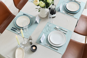 Elegant table setting for Nobel prize day with microscope, flowers and candles in dining room