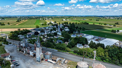 A small rural town surrounded by green fields under a blue sky filled with clouds. The town has...