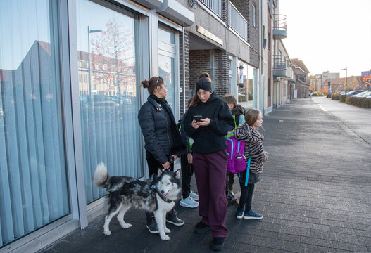 Family members and their Siberian husky dog waiting on a city sidewalk, one woman checking her smartphone, illustrating digital connection and urban pet ownership