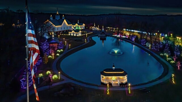 Colorful lights decorate trees and buildings around a calm lake as night falls. A gazebo stands by the water, with a fountain adding to the festive atmosphere, creating a peaceful winter scene. - Powered by Adobe