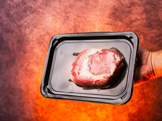 Premium top quality beef rib eye steak in black plastic vacuum packed package in butcher hand, red hot flaming fire background. High value and cost meat product with expensive price.