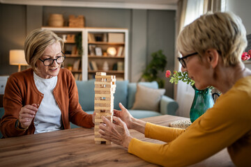 Senior women friends playing jenga board game at home
