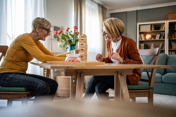 Senior women friends playing jenga board game at home