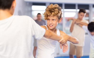 Obraz premium Diligent preteen student practicing self-defense techniques in pairs during workout session