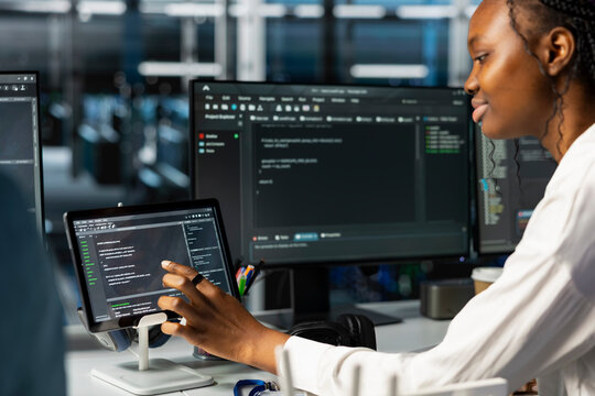 Data center female technician using tablet, coding, managing systems for uptime and efficiency. African american woman pressing device touchscreen, using programming languages in server hub - Powered by Adobe