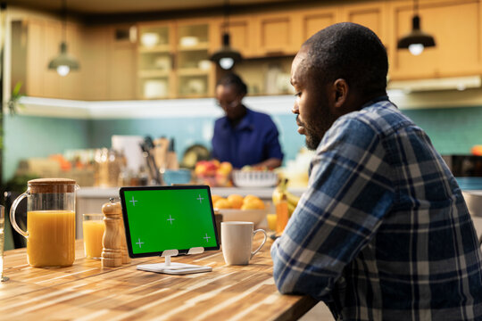 Green screen mockup on tablet with African American man enjoying breakfast at the table while partner prepares the meal. Representing modern lifestyle, technology and togetherness.
