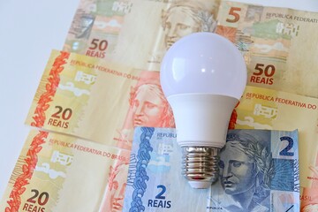 Conta de Luz (electricity bill in Portuguese) post-it reminder stuck on a light bulb, Brazilian Real banknotes and calculator. Electricity bill in Brazil concept.