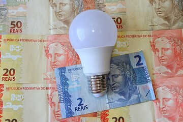 Conta de Luz (electricity bill in Portuguese) post-it reminder stuck on a light bulb, Brazilian Real banknotes and calculator. Electricity bill in Brazil concept.