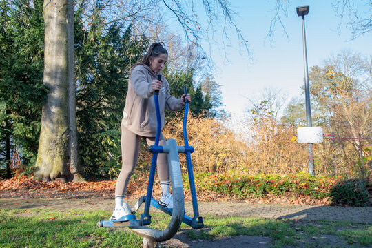 Young woman enjoying an outdoor workout session, exercising on an elliptical machine in a public park, embracing fitness and healthy living during autumn