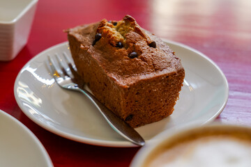 Delicious chocolate chip banana bread loaf served on a white plate with a fork, ready to be enjoyed with a coffee in a cozy cafe setting.