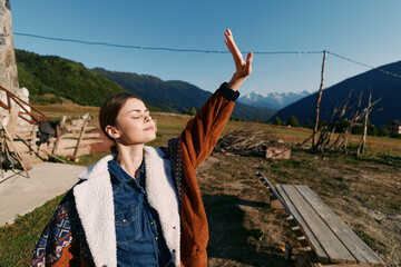 Fototapeta premium woman nature mountains sunlight outdoors portrait rural freedom enjoying fresh air with closed eyes and raised hand on a sunny day at a country farmhouse landscape for relaxation and wellbeing