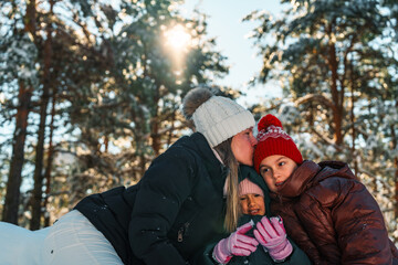 Obraz premium Happy loving family of mother and two daughters enjoying a sunny winter day in a snowy forest, wearing warm winter clothes, expressing tenderness and affection
