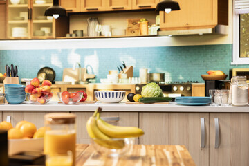 Empty kitchen with wooden dining furniture and modern appliances. Countertop displays colorful vegetables, fresh fruits and spices, representing a stylish home with cozy atmosphere.