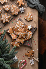 Christmas gingerbread cookies decorated with icing on rustic wooden board. Festive mood, cozy xmas home atmosphere, fir tree branches, top view