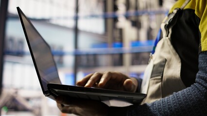 Close up of smart factory worker using laptop to test automated systems, monitoring production metrics. Industry 4.0 plant expert inspecting machinery to identify and fix malfunctions, camera A