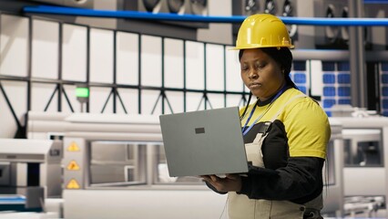 Technician in eco friendly industrial plant monitors production equipment using notebook, diagnosing malfunctions. Factory employee coordinates repair tasks on solar panels assembly line, camera B