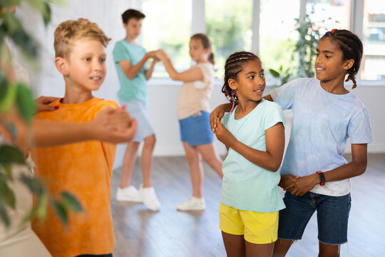 Group of positive juvenile boys and girls doing Tango poses in training room during workout session