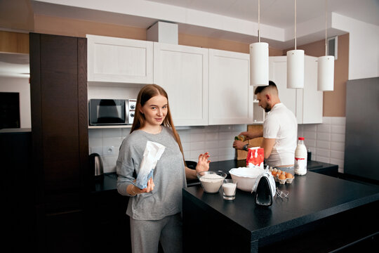 Couple cooking together in modern kitchen, preparing food with various ingredients and kitchen utensils during the daytime