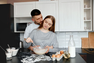 Couple cooking together in a kitchen while preparing a mixture in a bowl and enjoying time in each others company
