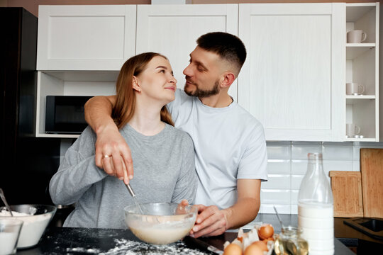 Couple prepares food together in a kitchen while sharing smiles and enjoying their time on a weekend morning