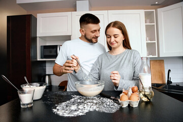 Couple cooking together in kitchen while preparing batter for baking on a sunny afternoon