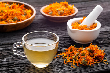 Cup of calendula tea, accompanied by dried petals and a white mortar with calendula flowers - Calendula officinalis