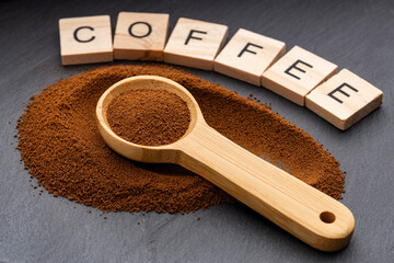 Close-up image of ground coffee with a wooden spoon and wooden letters spelling COFFEE