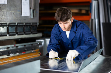 Young guy worker measures sheet of metal with tape measure in metallurgical workshop © JackF
