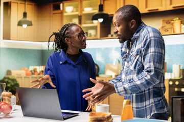 Black couple yelling at each other in a heated argument in a modern kitchen. Man gestures in anger while the woman expressing hurt and disappointment, relationship conflict and distress.